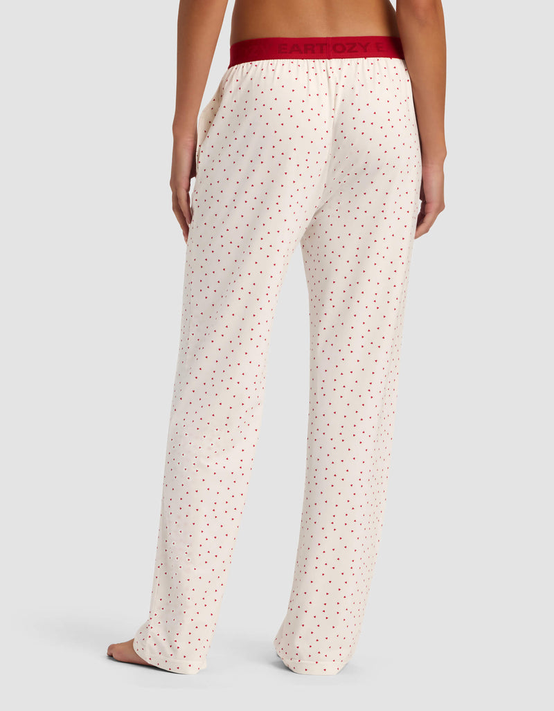 A person stands barefoot, facing away, wearing Cozy Earth Women's First Layer Pajama Pant in cream with small red polka dots and a burgundy waistband against a plain light background.