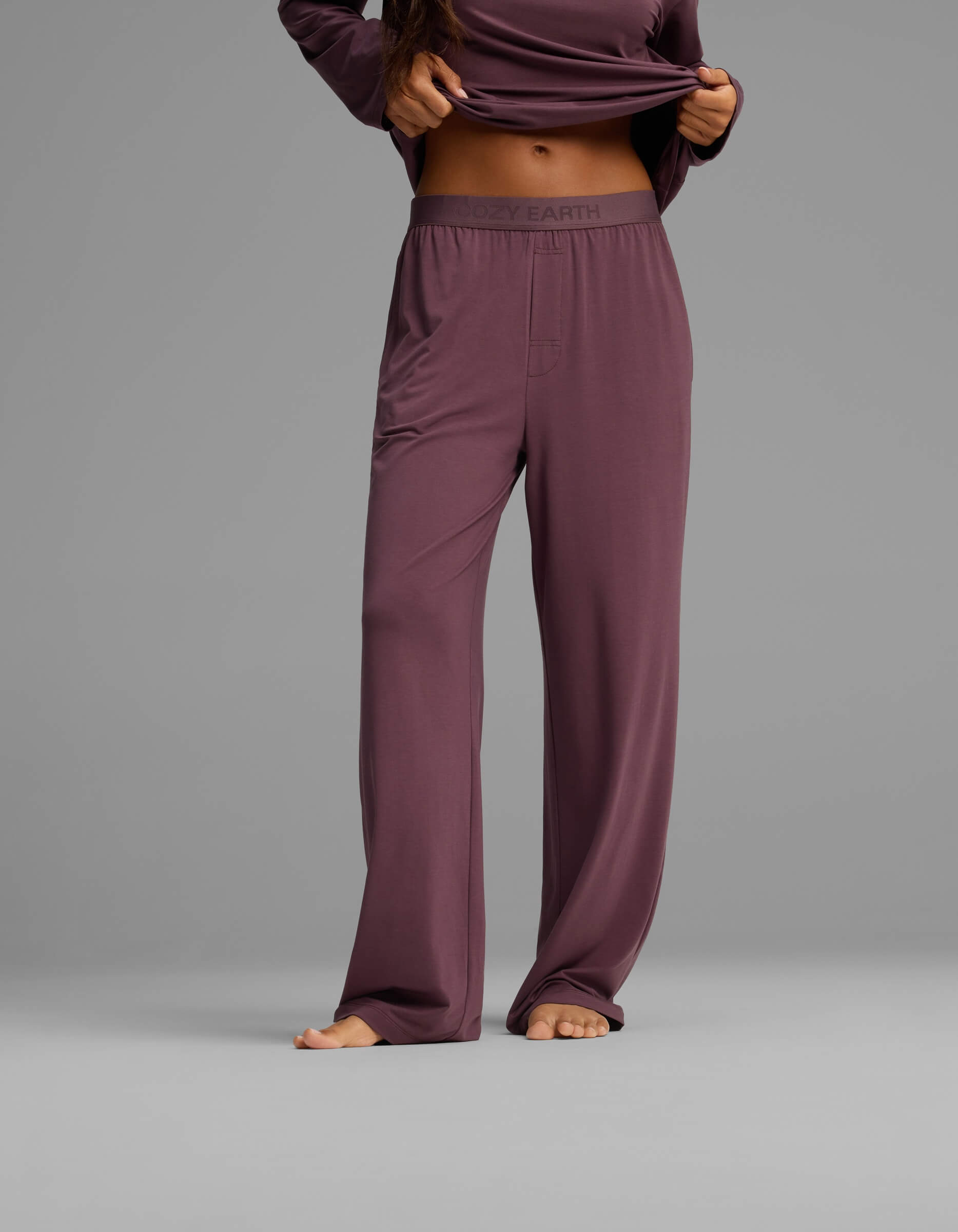 A person wears Cozy Earth’s Women’s First Layer Pajama Pant in mauve, standing barefoot against a plain gray background. The top of the person’s head is not visible in the image.|Color:Fig