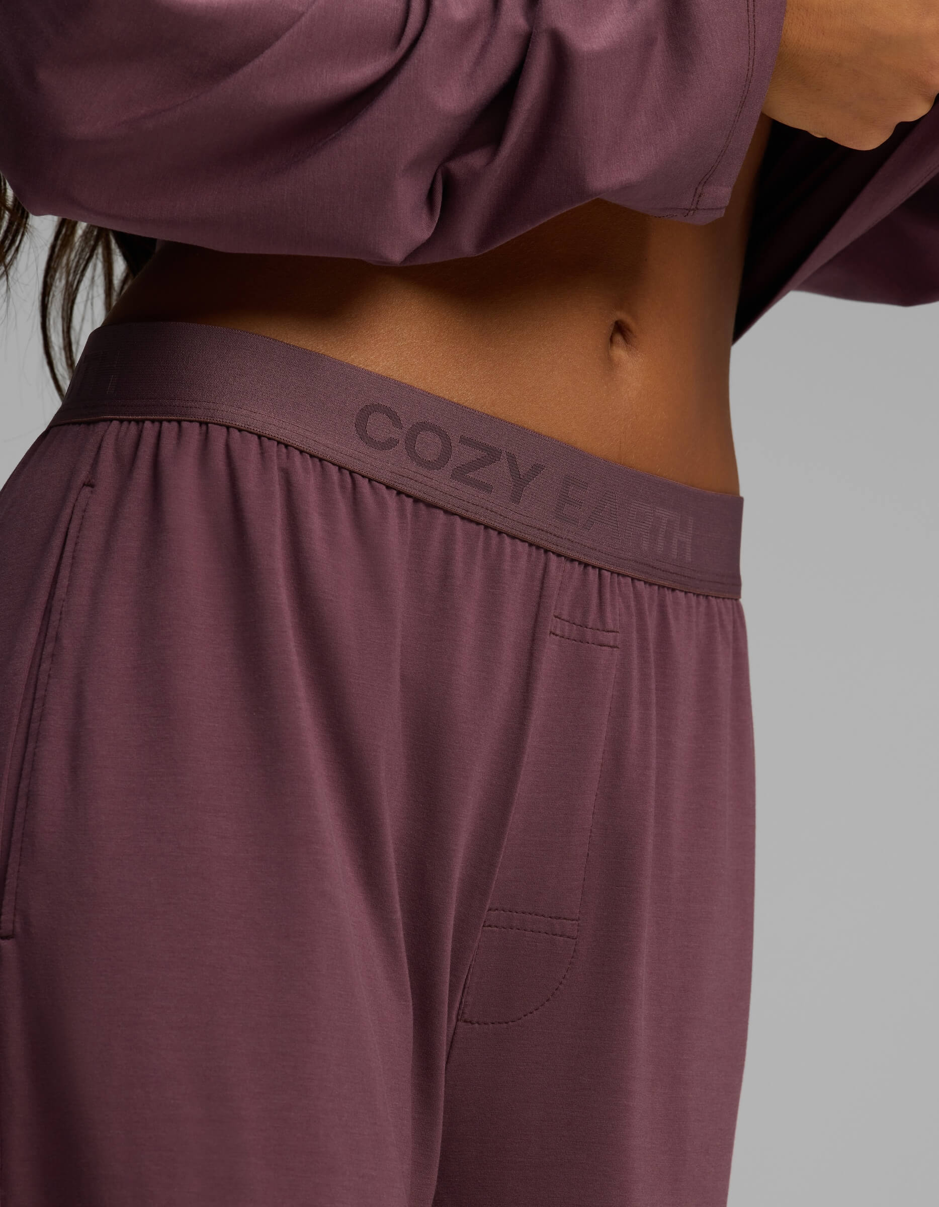 A close-up of a person wearing Cozy Earth Women’s First Layer Pajama Pants in mauve with a matching top, highlighting the waistband and partial midriff.