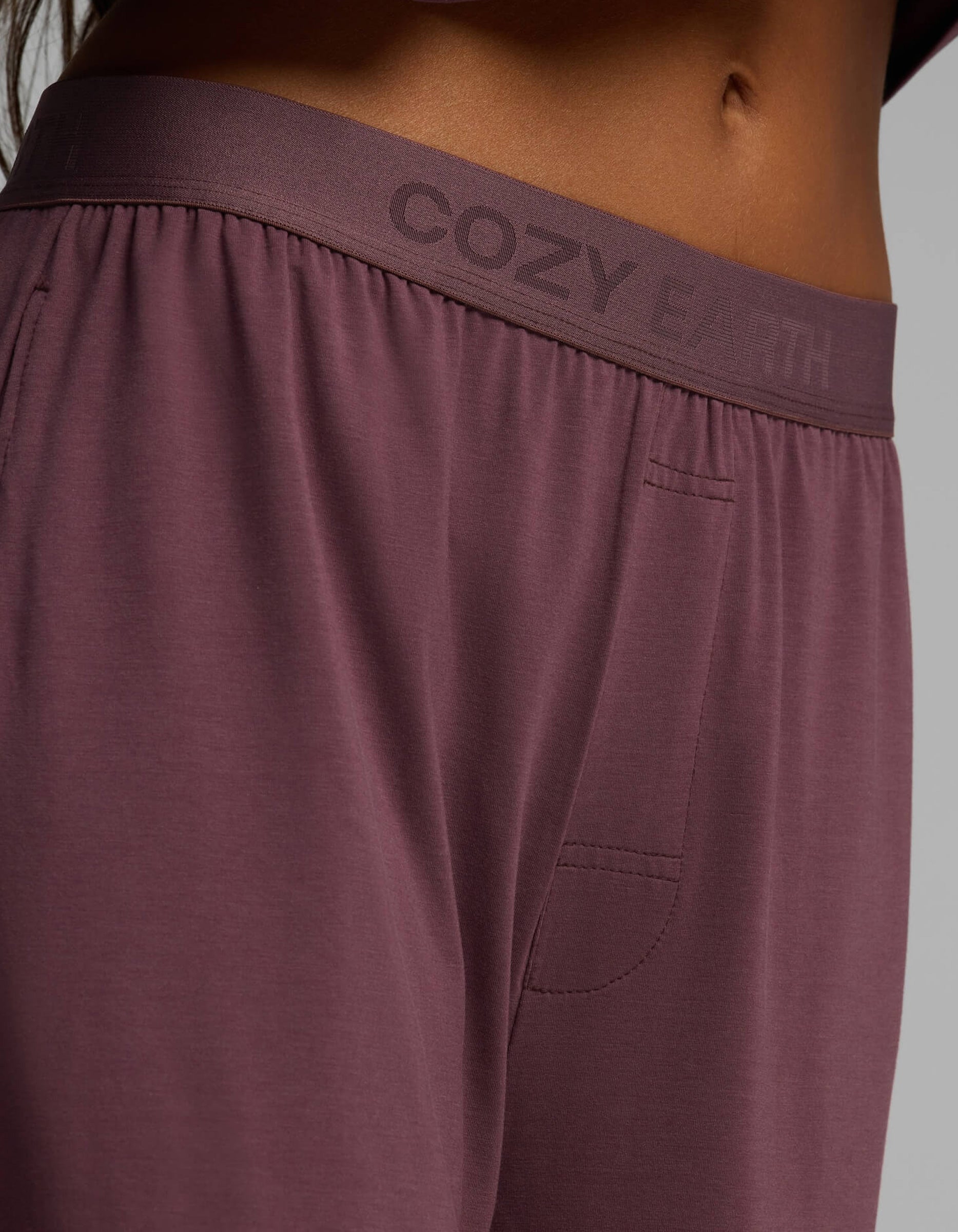 Close-up of a person wearing the Women’s First Layer Pajama Pant from Cozy Earth, featuring “COZY EARTH” printed on the waistband and a visible side pocket.