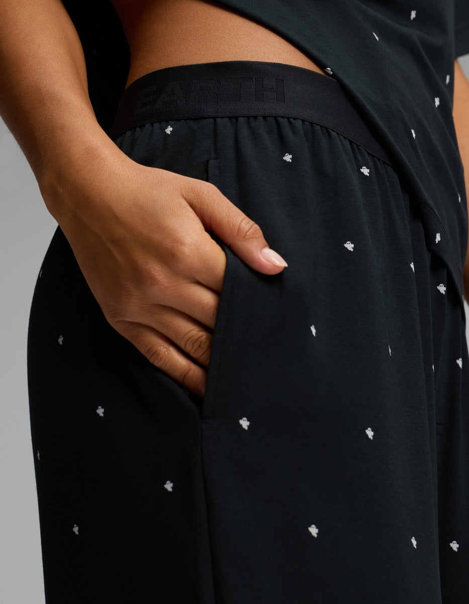Close-up of a person’s hand in the pocket of Cozy Earth Women’s First Layer Pajama Pant, featuring a black fabric with small white dot patterns. The waistband displays subtle branding, and the person pairs it with a matching black top.|Color:Mini Ghost
