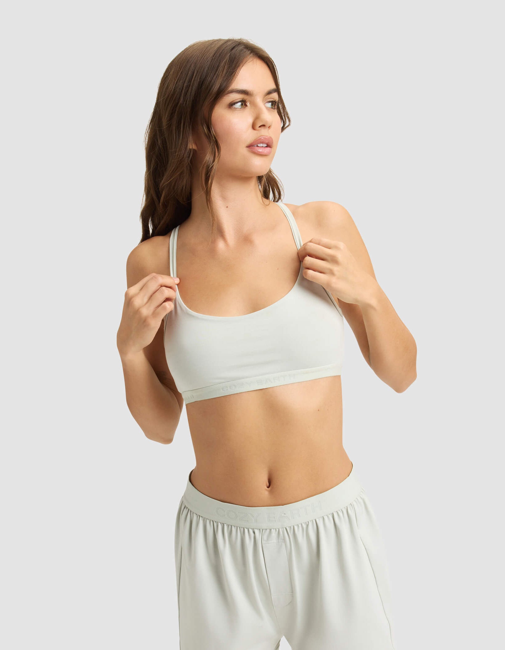 A woman with long brown hair models the Cozy Earth Women's First Layer PJ Soft Bra and matching shorts, standing against a plain light gray background and looking to the side.|Color:Laurel