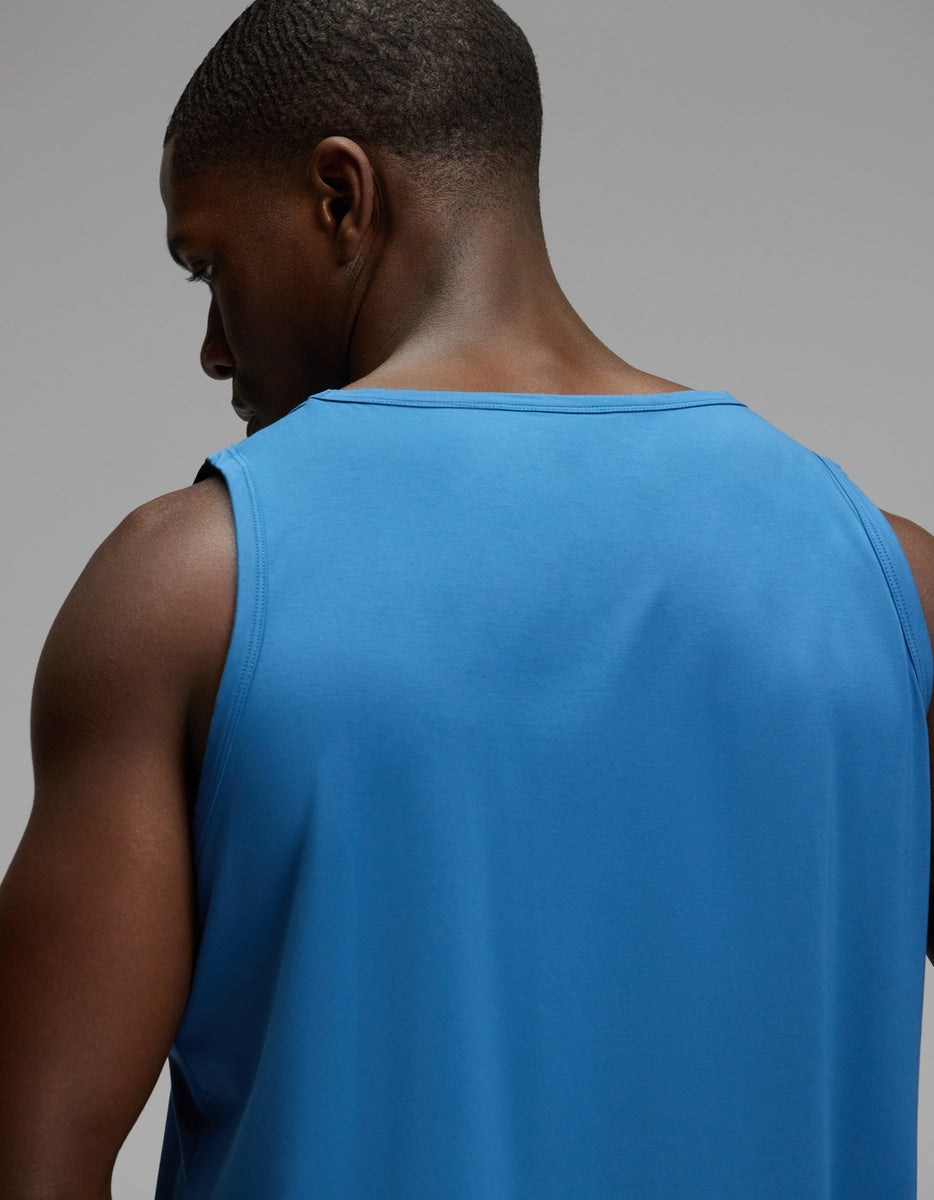 A man wearing the Cozy Earth Men’s First Layer Pajama Tank in blue is seen from behind, looking slightly to the left, against a plain gray background.