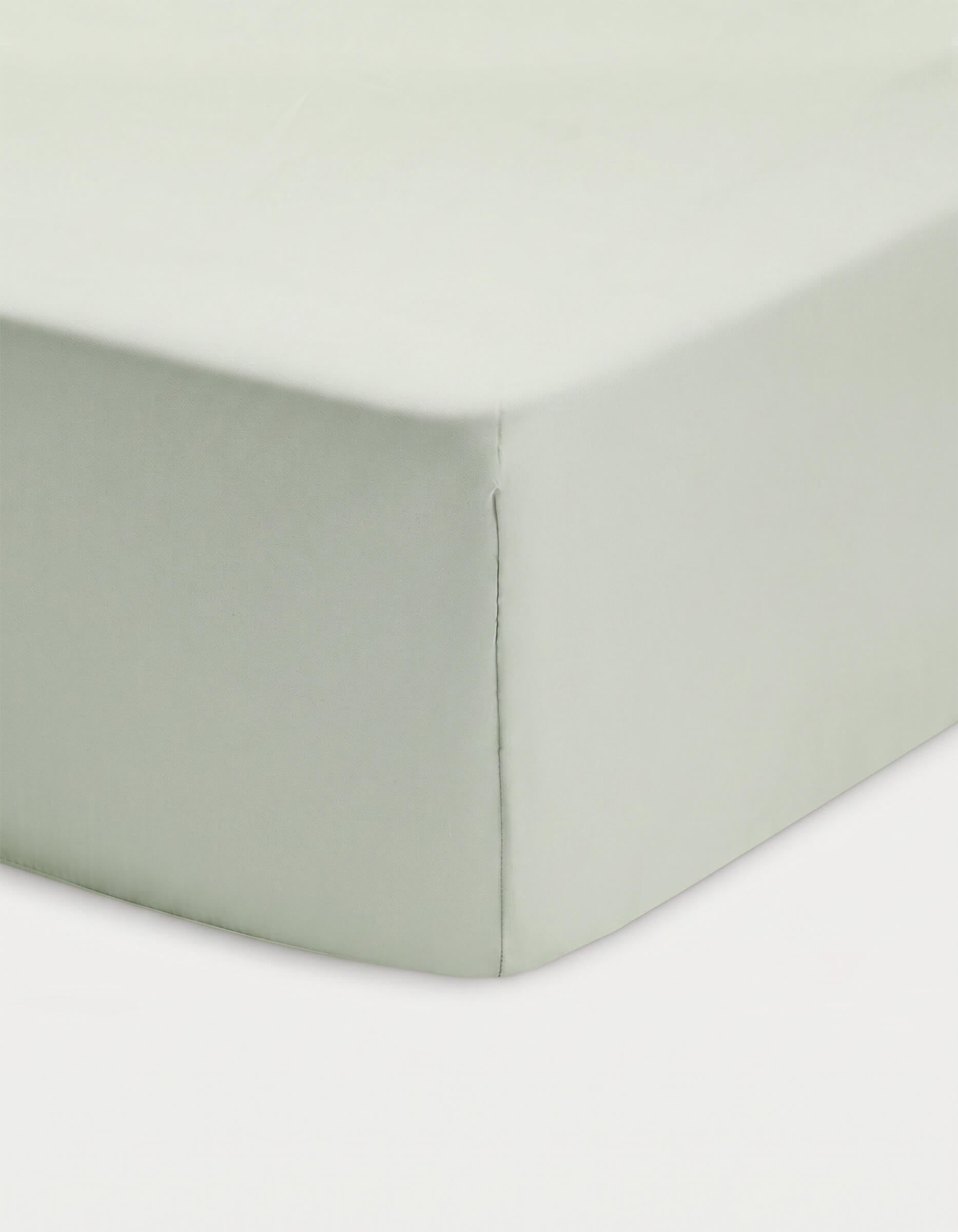 Close-up of a corner of a bed showcasing the Cozy Earth Bamboo Fitted Sheet in light green, neatly covering the mattress against a white background.