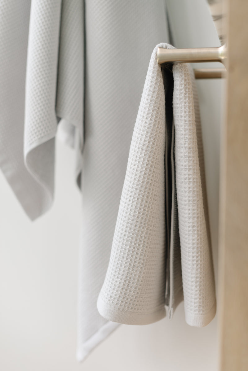 Waffle Hand Towel in the color Light Grey. Photo of Light Grey Waffle Hand Towel taken with the Light Grey Waffle Hand Towel hung from a towel ring. The picture was taken in a bathroom.