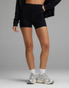 A person wearing black Women’s Liv Biker Short 4″, a black zip-up jacket, white crew socks, and metallic athletic sneakers.|Color:Jet Black