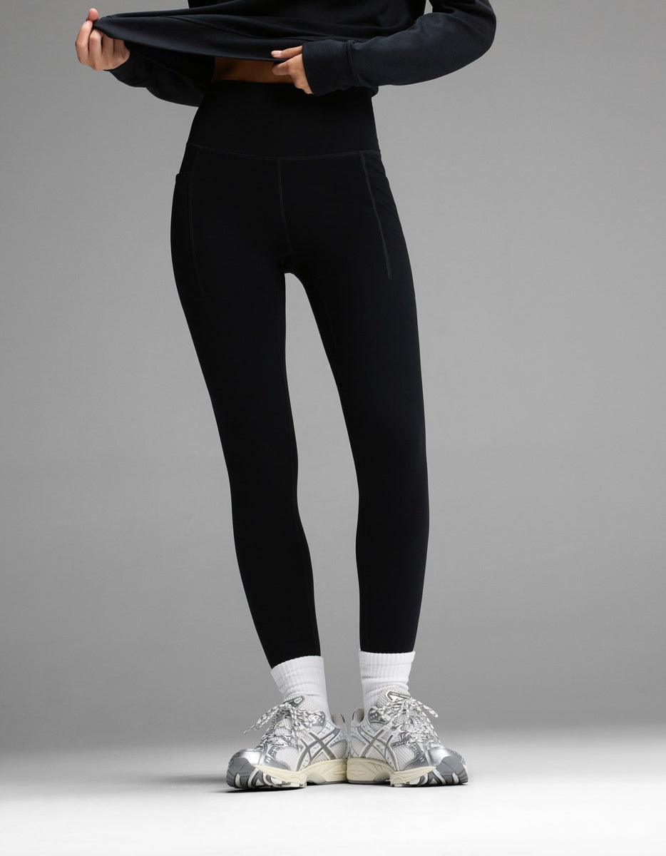A person wearing black Women’s Liv Leggings with Pockets, white socks, and silver running shoes.