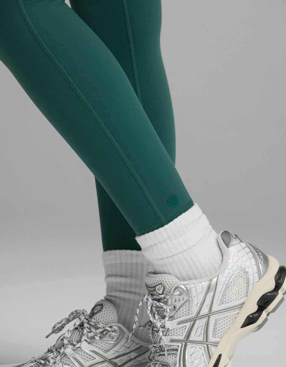 Close-up of dark green Women’s Liv Leggings with Pockets worn with white socks and silver athletic sneakers.