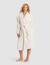 A woman stands barefoot against a light gray background, wearing the Cozy Earth Striped Luxe Bath Robe—white with beige vertical stripes and a belted waist.|Color:Sand Stripe