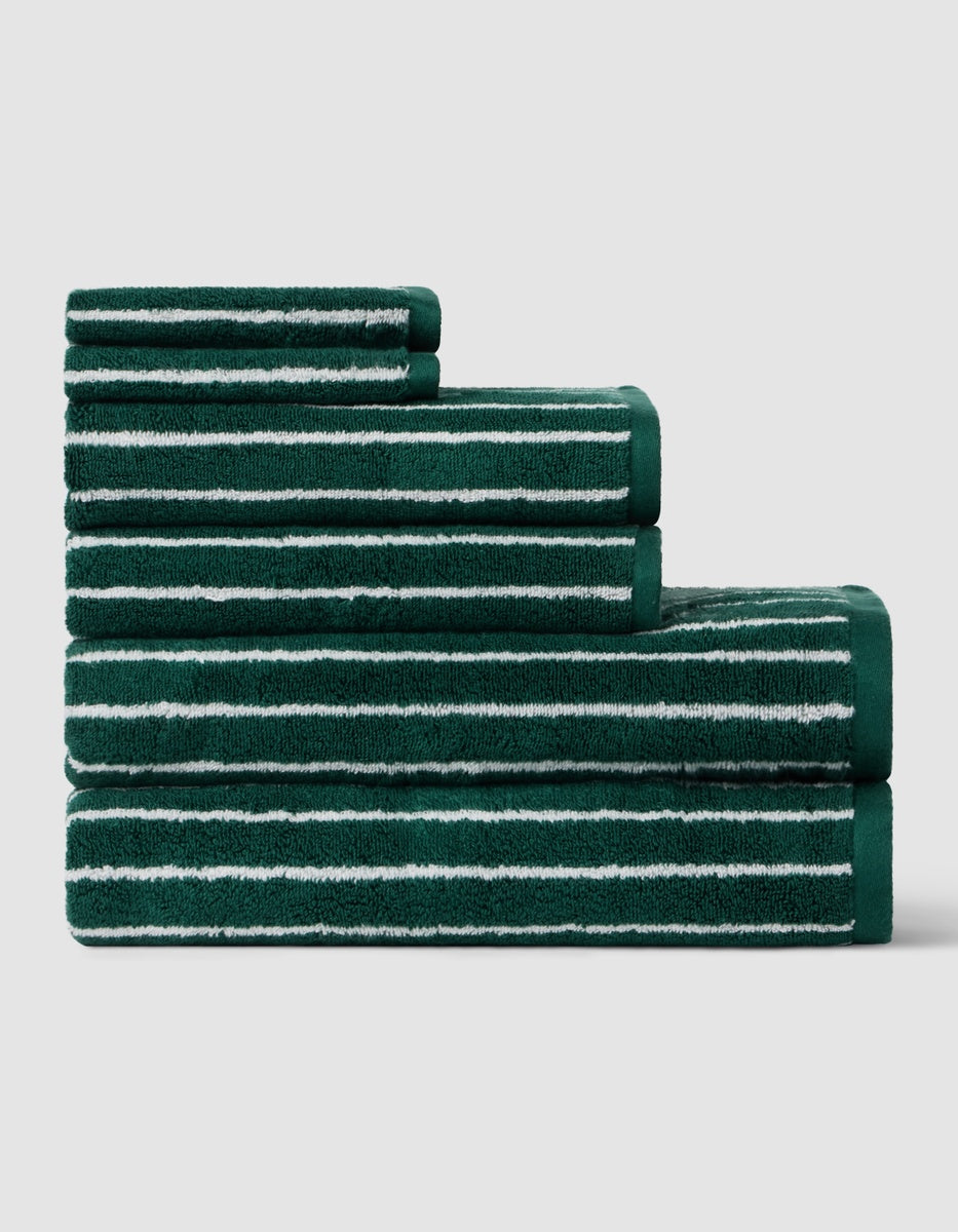 Four Luxe Bath Towel Set towels by Cozy Earth, stacked in ascending order, feature green fabric with horizontal white stripes against a plain light gray background.