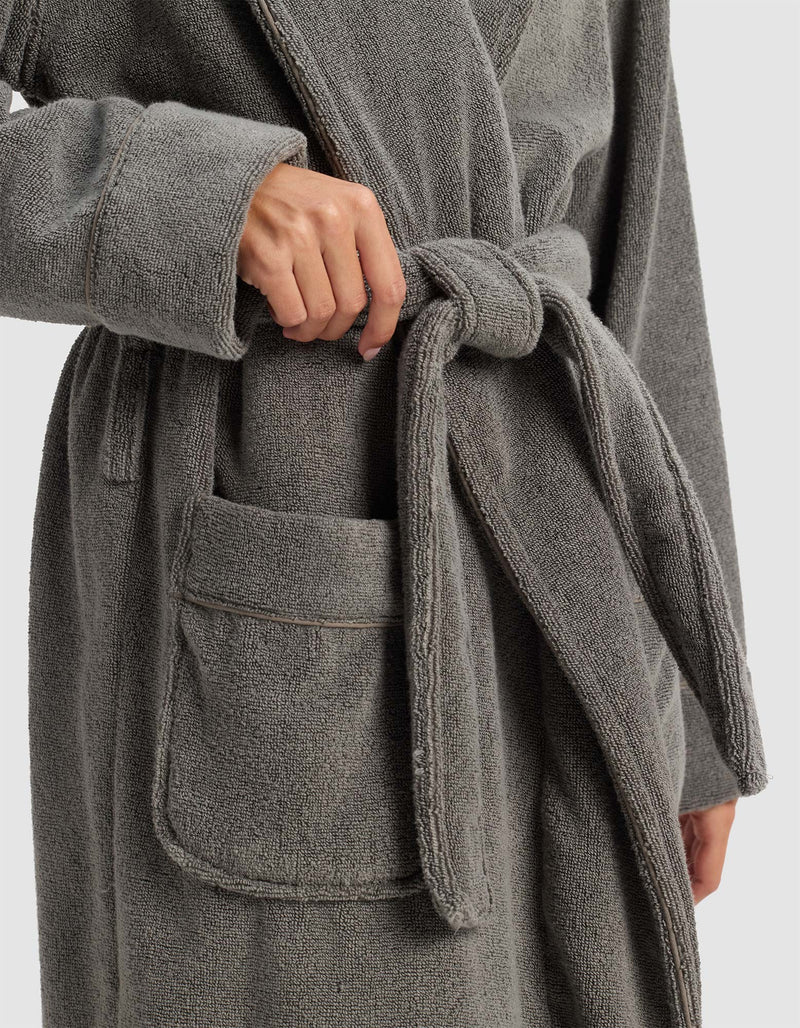 A person in the Cozy Earth Luxe Bath Robe ties the waist belt; one hand loops the belt, and the plush robe features a spacious front pocket.