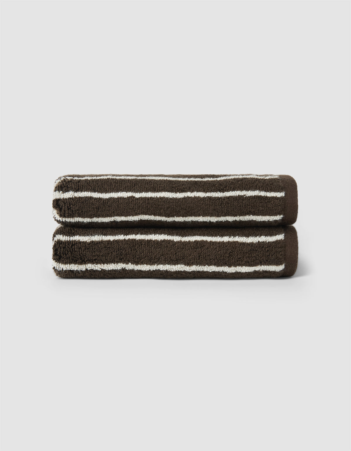 Two neatly rolled Striped Luxe Bath Towels by Cozy Earth, featuring dark brown with white horizontal stripes, are stacked atop each other against a plain light background.|Color:Espresso Coconut Stripe