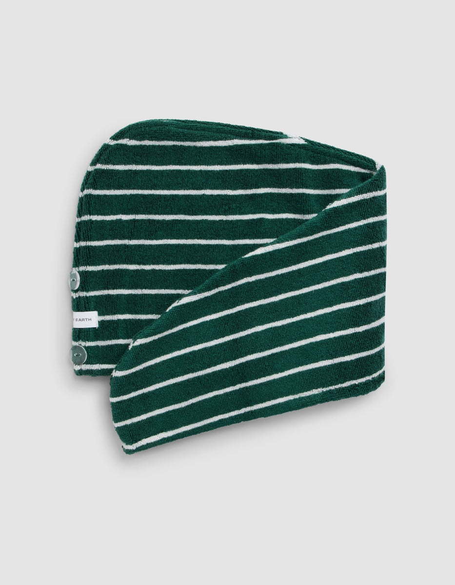 The Luxe Hair Towel by Cozy Earth features dark green and white stripes, two snap buttons, and a small white tag on the edge, folded to reveal both sides.