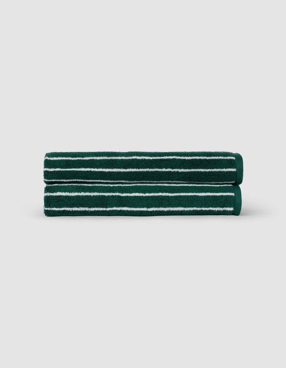 Two Luxe Hand Towels by Cozy Earth, dark green with white horizontal stripes, are neatly rolled and stacked against a plain light gray background.