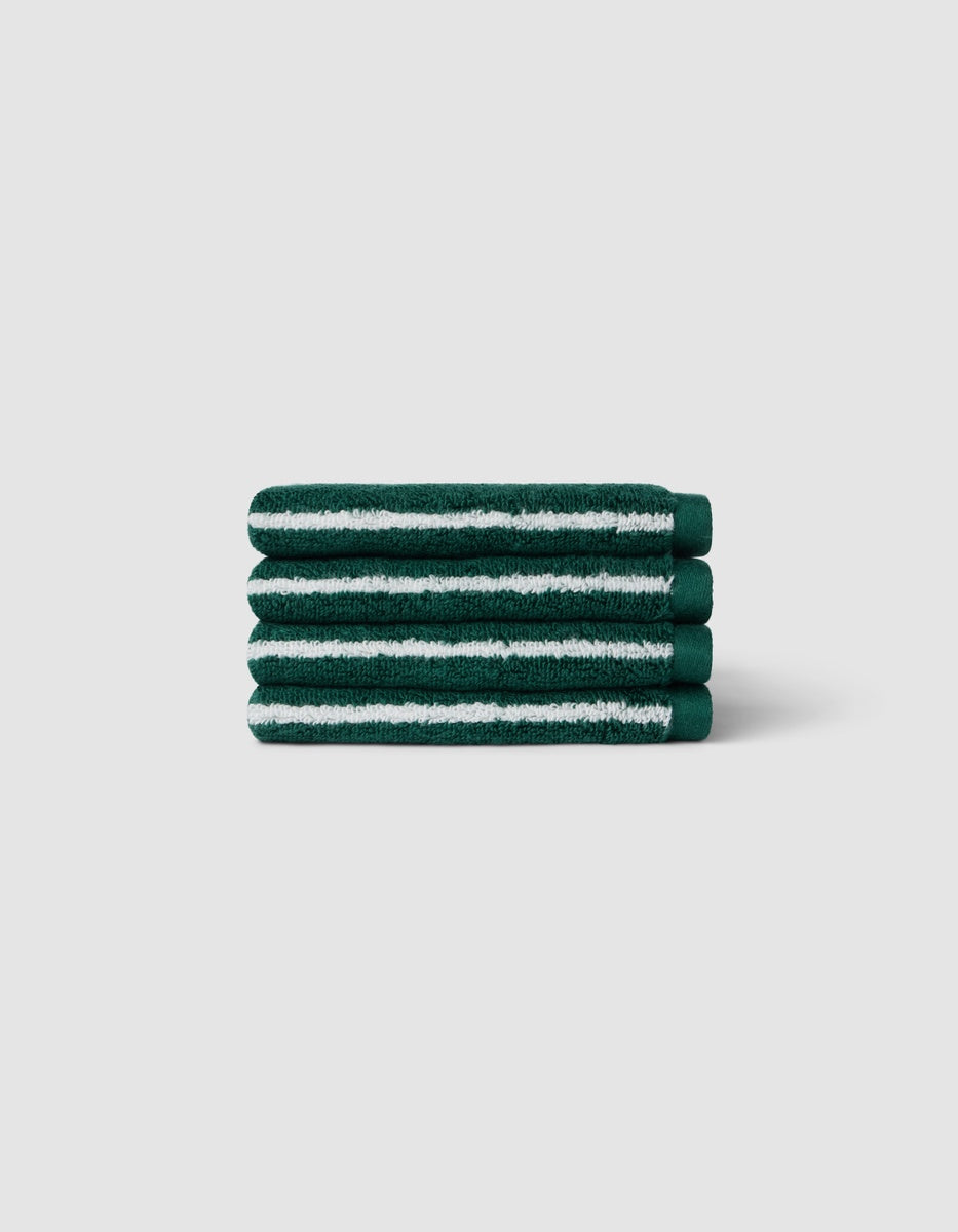 A stack of four Luxe Washcloths by Cozy Earth in dark green with white stripes, displayed against a light gray background.