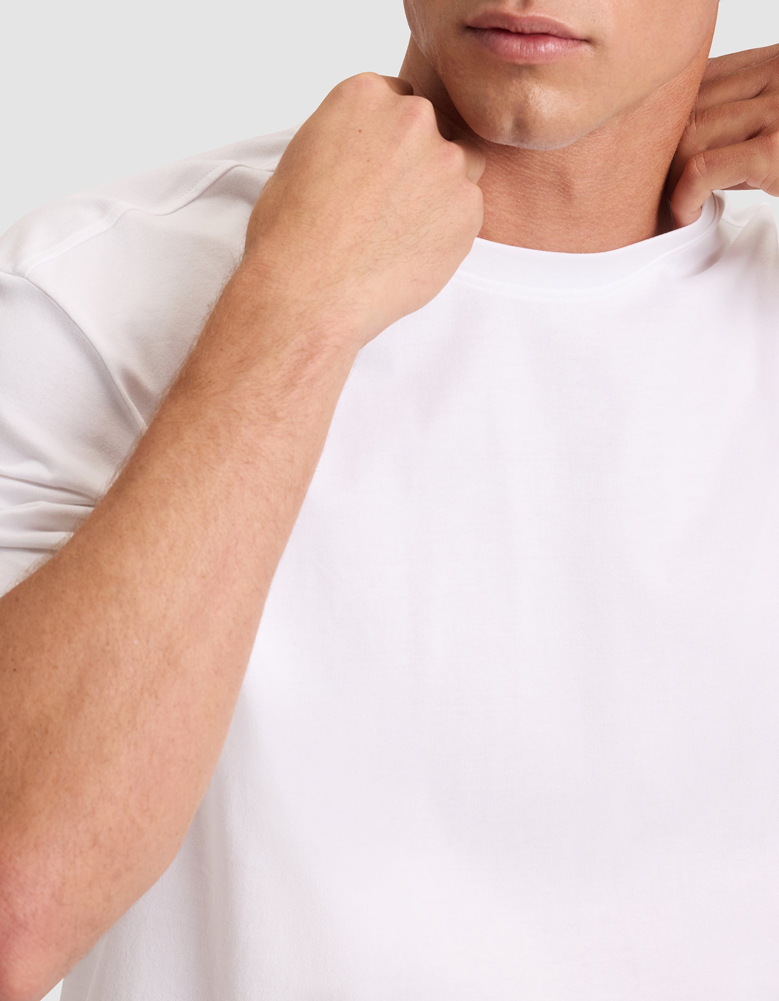 A close-up of a man wearing Cozy Earth's Men's All Day Tee in plain white, adjusting the collar with both hands against a neutral background. His face is partially visible. 