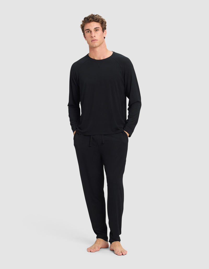 A man stands barefoot against a plain light gray background, wearing the Cozy Earth Men's Bamboo Stretch-Knit Long Sleeve and matching drawstring pants, with his hands in his pockets.