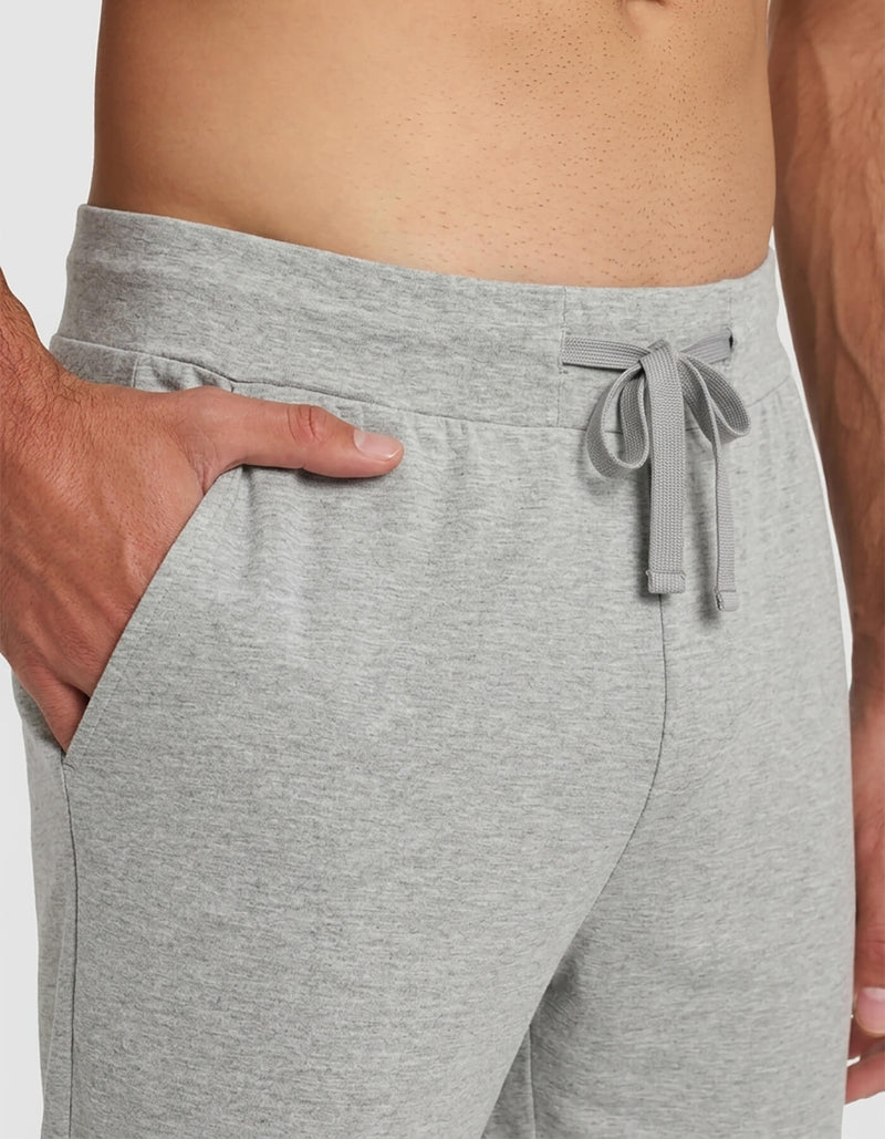 A close-up of a person wearing Cozy Earth's Men's Bamboo Stretch-Knit Short Sleeve Pajama Set, featuring light gray drawstring waist pants with one hand in the pocket and a bare torso visible.