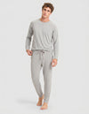 A person stands barefoot against a plain light background, wearing the Cozy Earth Men's Bamboo Stretch-Knit Long Sleeve Pajama Set in Heather Grey.|Color:Heather Grey