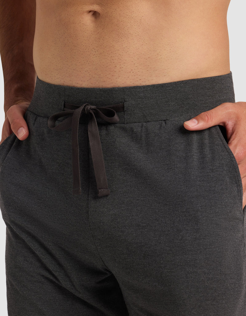 A close-up of a person wearing Cozy Earth's Men's Bamboo Stretch-Knit Pajama Short in dark gray, with hands in the pockets. The shirtless model is shown from waist to upper thighs, highlighting the comfortable stretch-knit fabric.