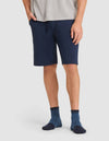 A person stands against a plain light background wearing Cozy Earth's Men's Bamboo Stretch-Knit Pajama Short in navy blue, paired with a gray t-shirt and dark blue socks, with one hand in their pocket. |Color:Navy