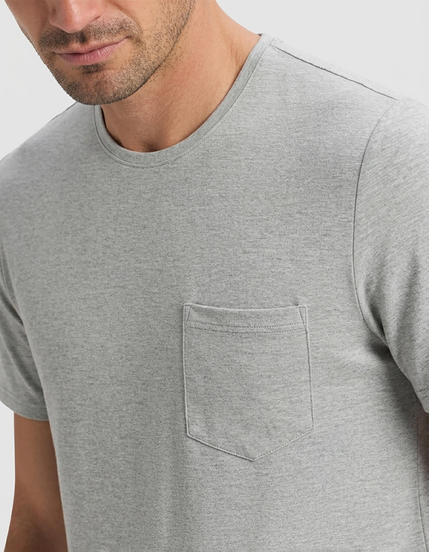 A man is shown from shoulders to mid-torso, facing slightly sideways, wearing the Cozy Earth Men's Bamboo Stretch-Knit Short Sleeve Pajama Set in light gray with a chest pocket against a plain background.