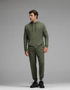 A man models the Cozy Earth Men’s Brushed Bamboo Hoodie & Jogger Set in olive, standing against a plain gray background. He looks slightly to his left with his hands relaxed at his sides, completing the look with black sneakers.|Color:Olive
