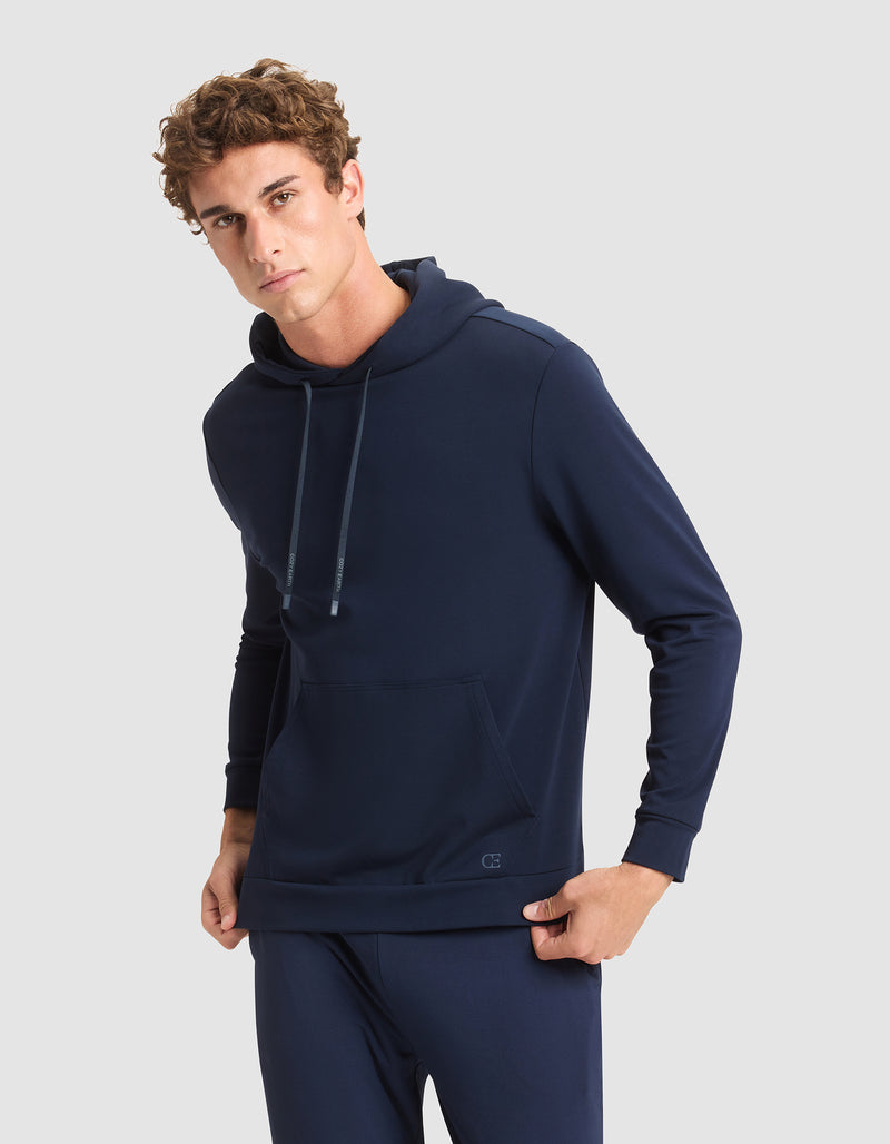 A young man wears the Cozy Earth Men's Brushed Bamboo Hoodie in navy blue, paired with matching pants, standing against a plain light gray background and looking at the camera with a neutral expression.