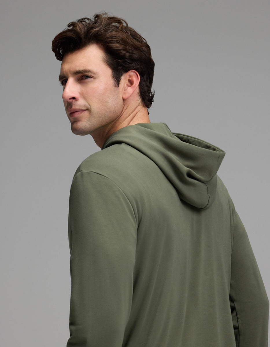 A man with short brown hair models the Cozy Earth Men’s Brushed Bamboo Hoodie in olive green, glancing over his shoulder against a plain gray background.