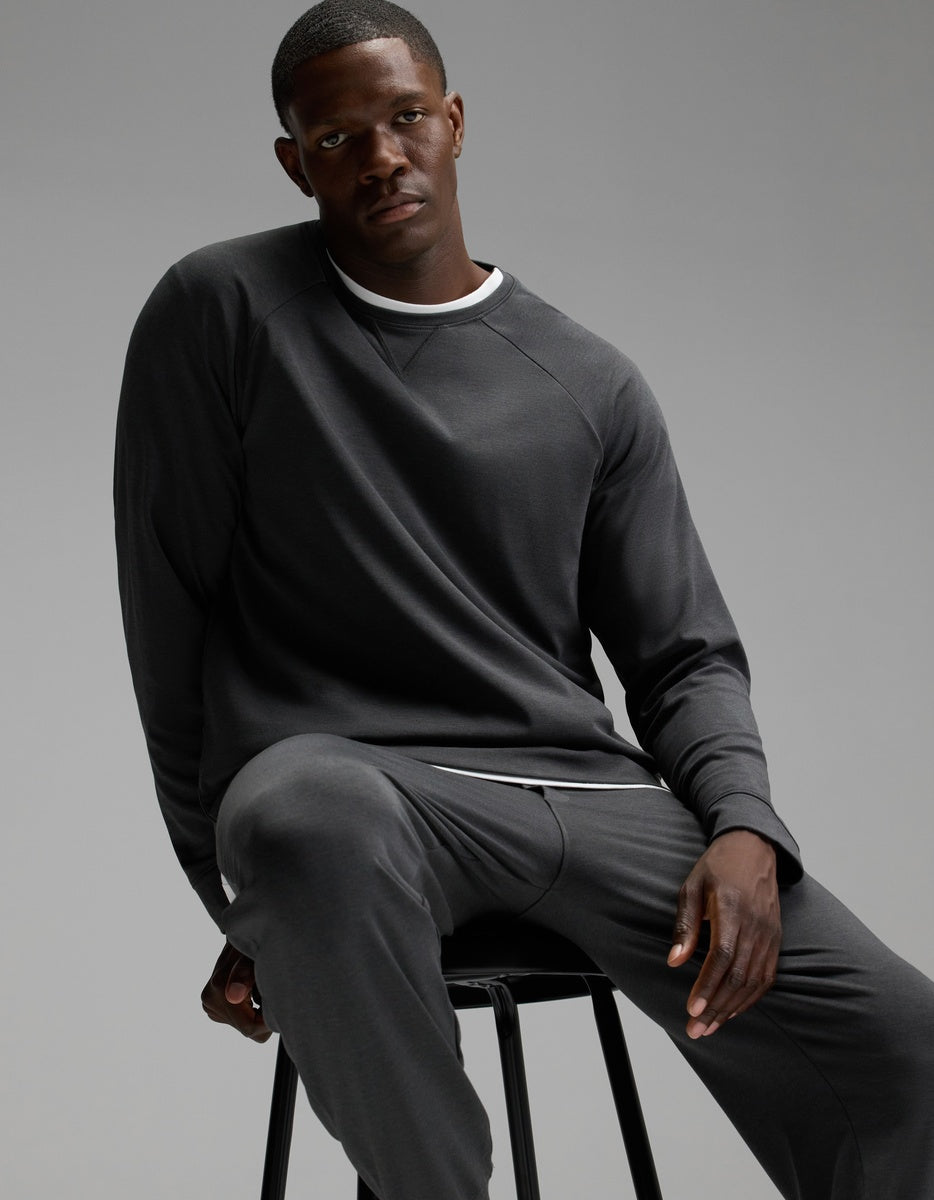 A man wearing Cozy Earth Men’s Brushed Bamboo Joggers in dark gray sits on a black stool against a plain gray background.