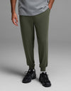 A person wearing Cozy Earth Men’s Brushed Bamboo Joggers in olive green, paired with black sneakers and a gray T-shirt, stands against a plain gray background. Only the lower half of their body is visible.