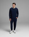A man is seen standing against a plain gray background wearing the Cozy Earth Men’s Brushed Bamboo Jogger Set in navy blue, paired with white sneakers and a white shirt underneath. He looks slightly to his left with one hand in his pocket.|Color:Navy
