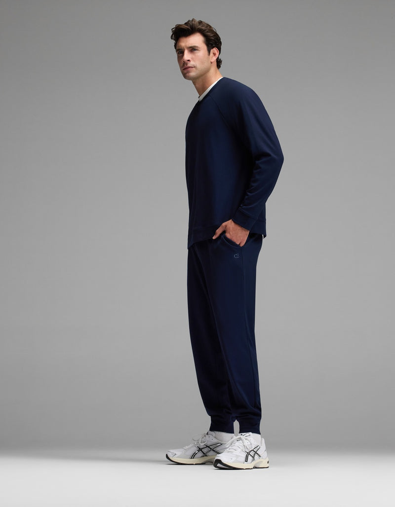 A man stands sideways against a plain gray background, wearing the Cozy Earth Men’s Brushed Bamboo Jogger Set in dark blue, paired with white sneakers.
