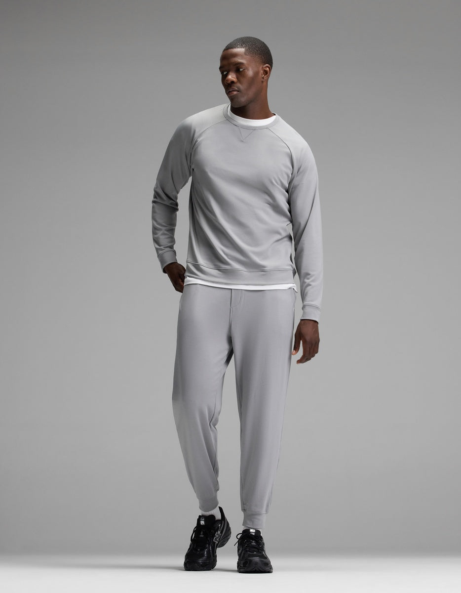 A man stands against a plain gray background wearing the Cozy Earth Men’s Brushed Bamboo Jogger Set in light gray, paired with black sneakers, looking to his left with one hand in his pocket.