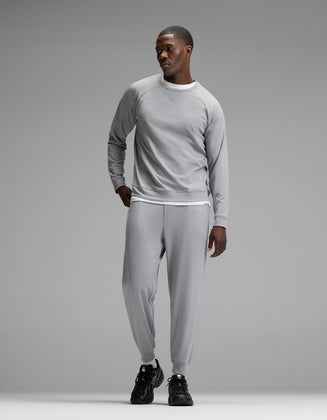 A man stands against a plain gray background wearing the Cozy Earth Men’s Brushed Bamboo Jogger Set in light gray, paired with black sneakers, looking to his left with one hand in his pocket.|Color:Stone