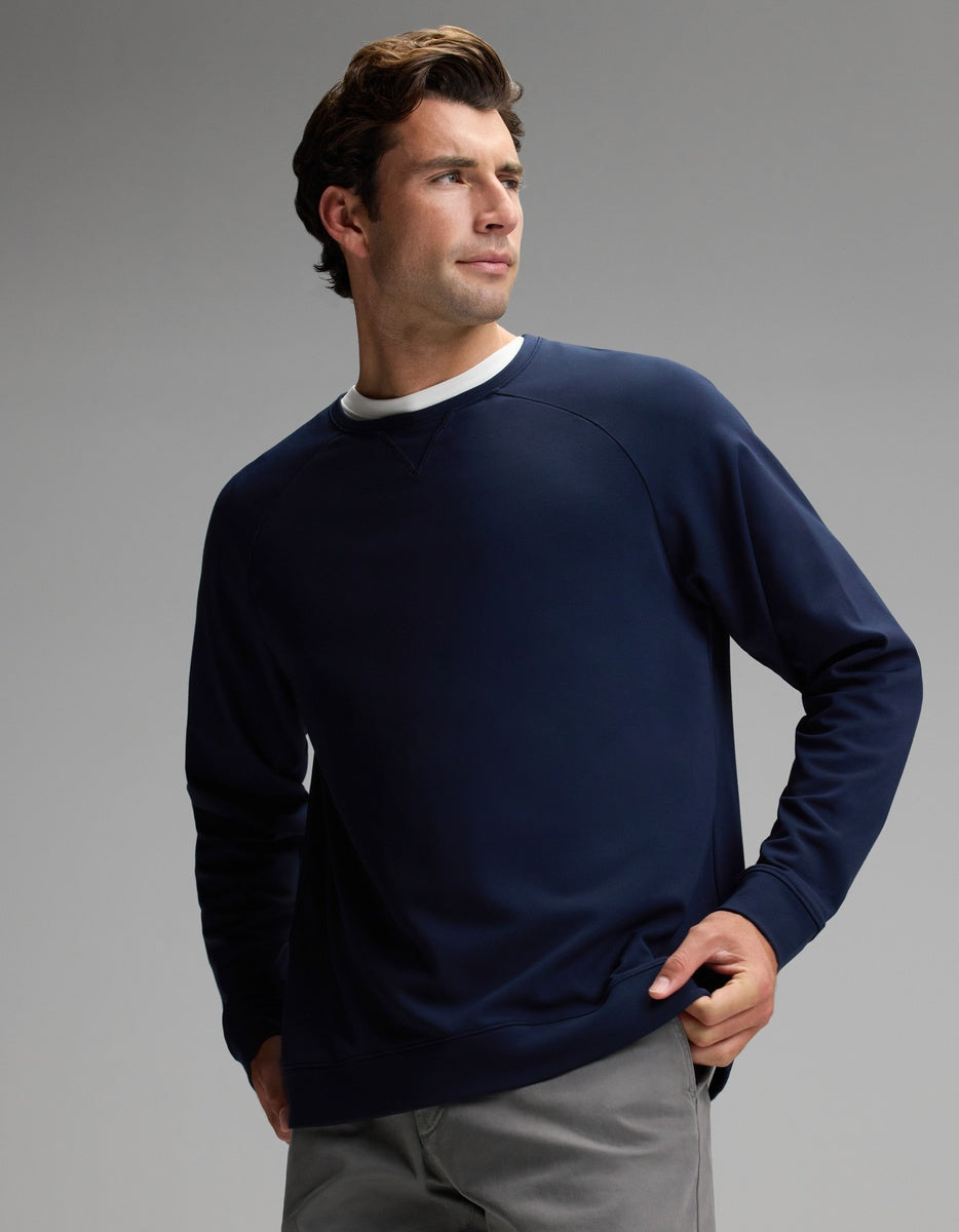 A man wears the Cozy Earth Men’s Brushed Bamboo Pullover Crew in navy, paired with gray pants, as he stands against a plain gray background and looks off to the side with one hand in his pocket.|Color:Navy