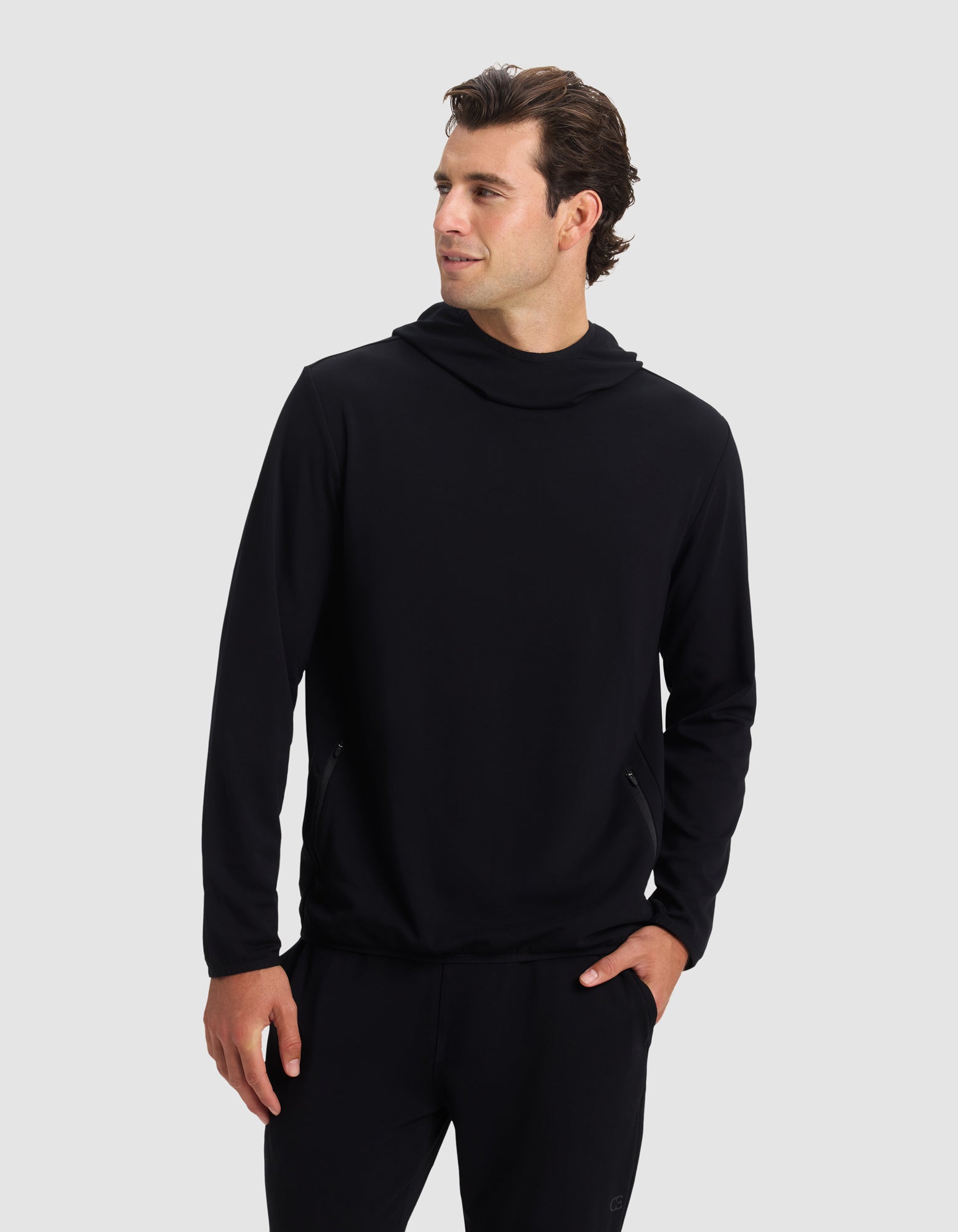 A man wears the Cozy Earth Men's Brushed Bamboo Recovery Hoodie and black pants, standing with one hand in his pocket and looking left against a plain light gray background. 