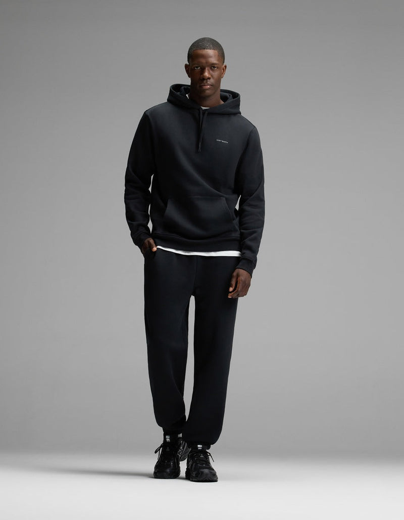 A man wearing Cozy Earth’s Men’s Cityscape Hoodie & Sweatpant Set in Jet Black stands against a plain gray background, facing the camera with a neutral expression.