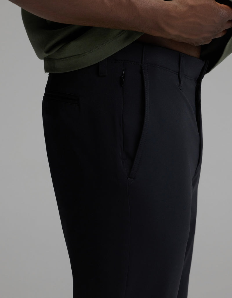 A person wearing Cozy Earth’s Men’s Everywhere Pant in black and a green shirt stands with one hand near the waistband, highlighting a close-up side view of the pant’s pocket and tailored fit.