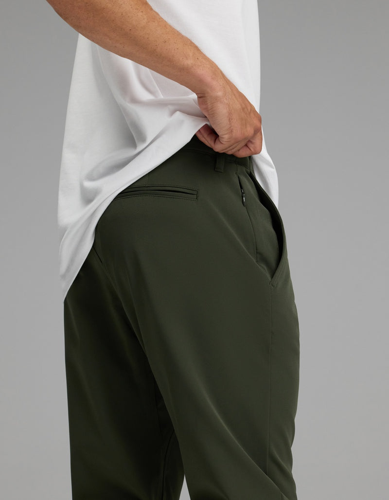A person wearing Cozy Earth’s Men’s Everywhere Pant in dark green stands with one hand in their pocket against a plain background.