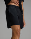 A person wearing Cozy Earth’s Men’s First Layer Pajama Short in Jet Black, paired with a matching black shirt, stands against a plain gray background with one hand resting on their waist.|Color:Jet Black