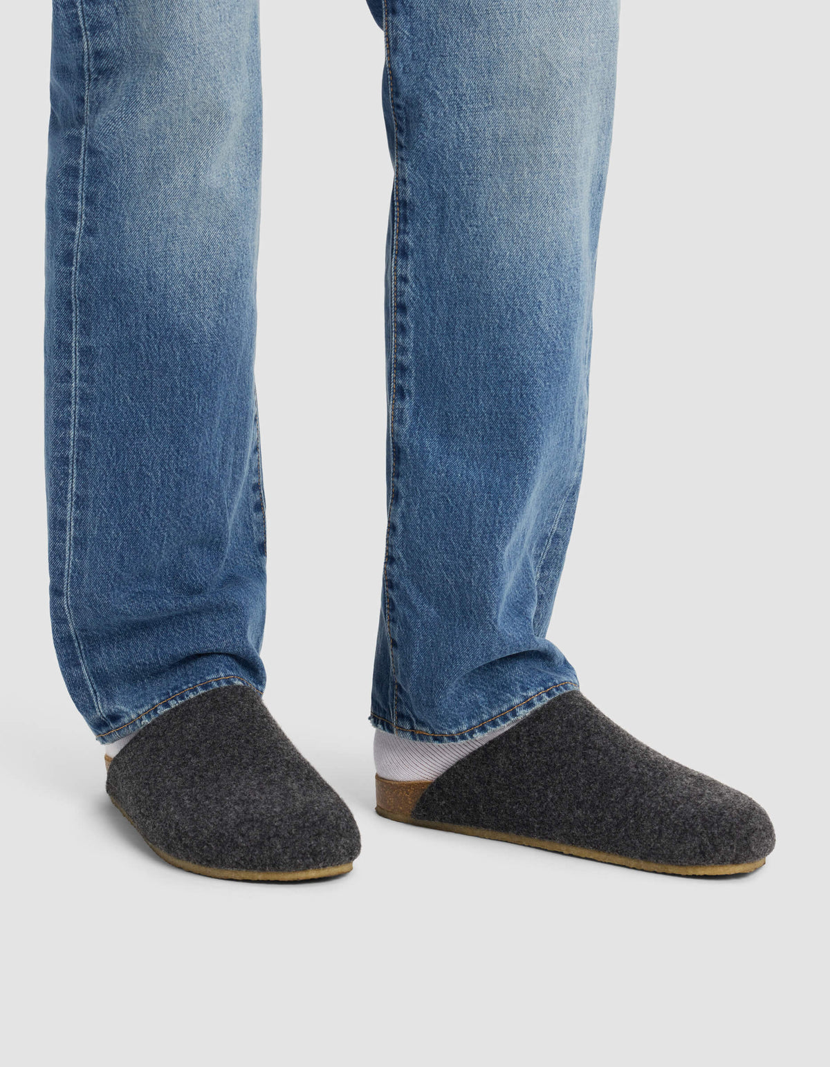 A person wears Cozy Earth's Lakehouse Clog slippers with blue jeans, standing on a light background. Only the lower legs and feet are visible.|Color:Graphite