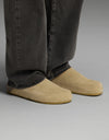A person wearing loose, dark-colored pants and Cozy Earth’s Lakehouse Clog in Suede stands on a light gray surface.|Color:Sandalwood