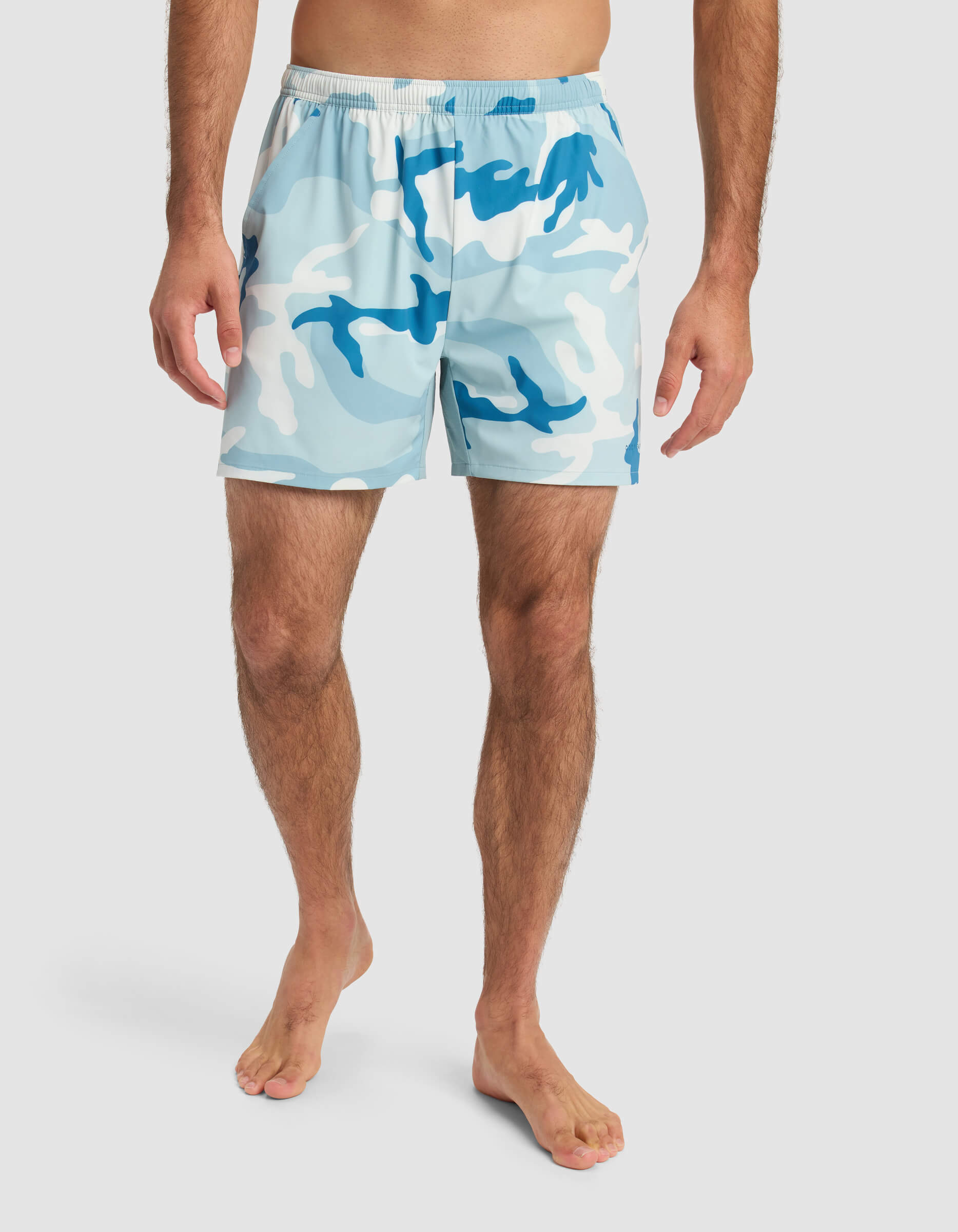 A barefoot man models Cozy Earth’s Men’s Day & Night Short 5" in a light blue, white, and dark blue camo print with an elastic waistband. His upper body is out of frame against a plain white background.|Color:Tide Camo