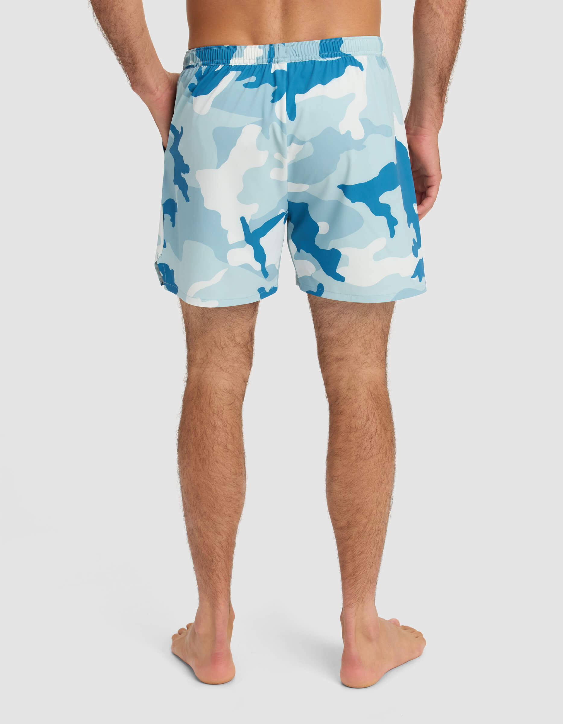 A person stands barefoot, facing away from the camera, wearing Cozy Earth Men's Day & Night Short 5" in blue and white camo. The background is plain and light-colored.|Color:Tide Camo
