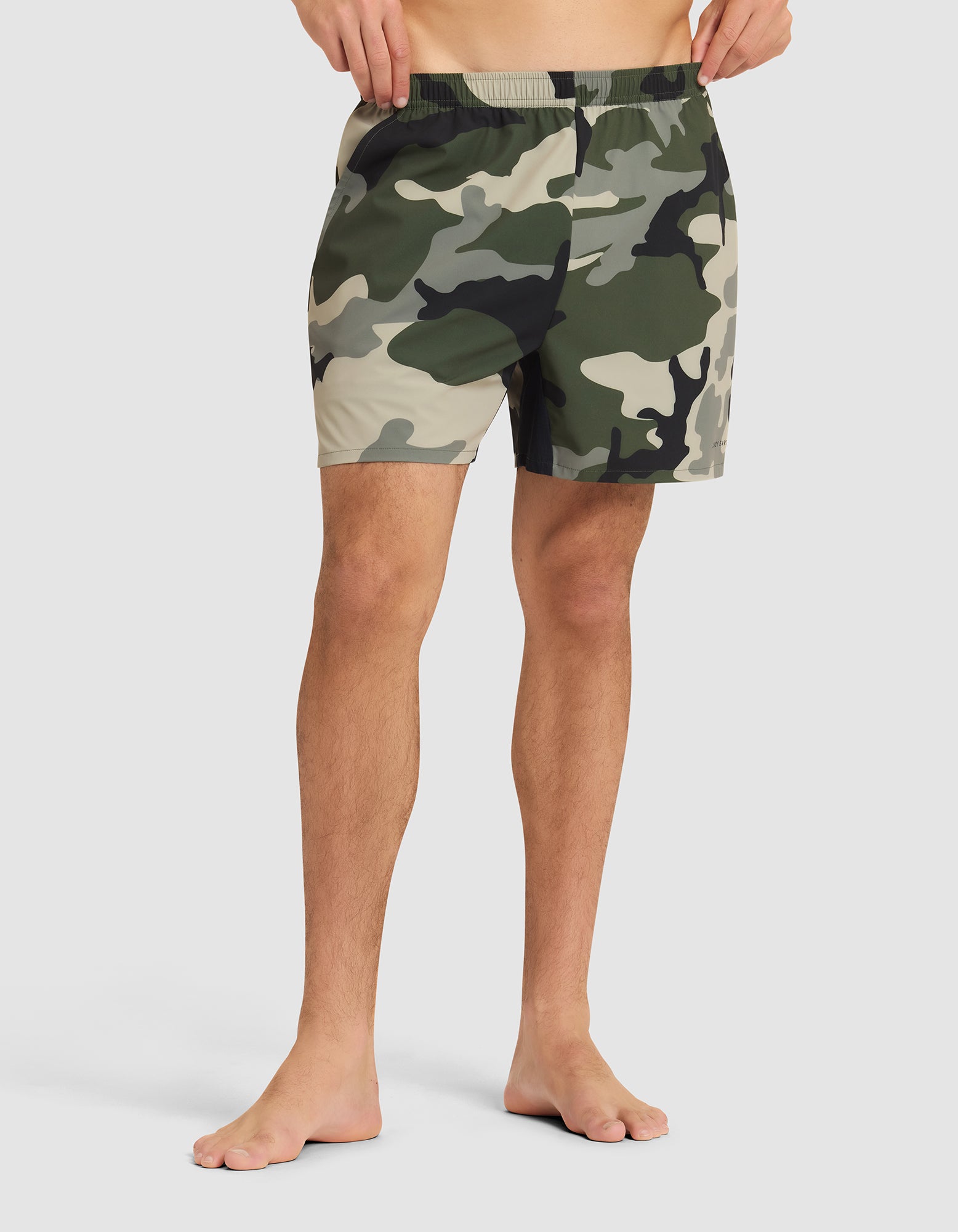 A person stands barefoot in Cozy Earth Men's Day & Night Shorts 5" against a plain light background, showing only the lower torso and legs. |Color:Cypress Camo