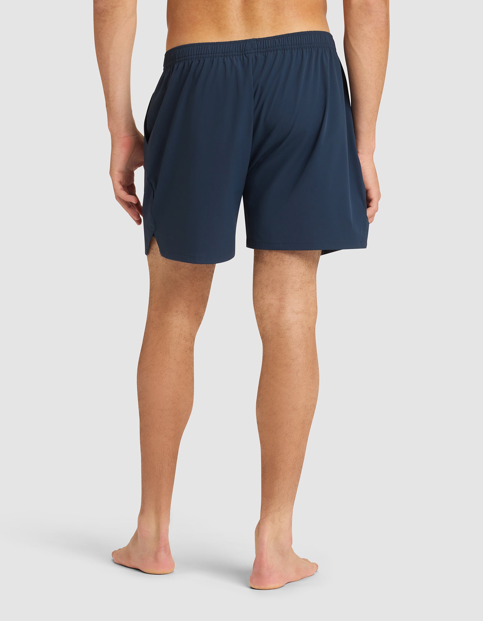 A person stands barefoot facing away, wearing Cozy Earth Men's Day & Night Shorts 5" in navy with an elastic waistband and side slits, set against a plain light background. |Color:Eclipse