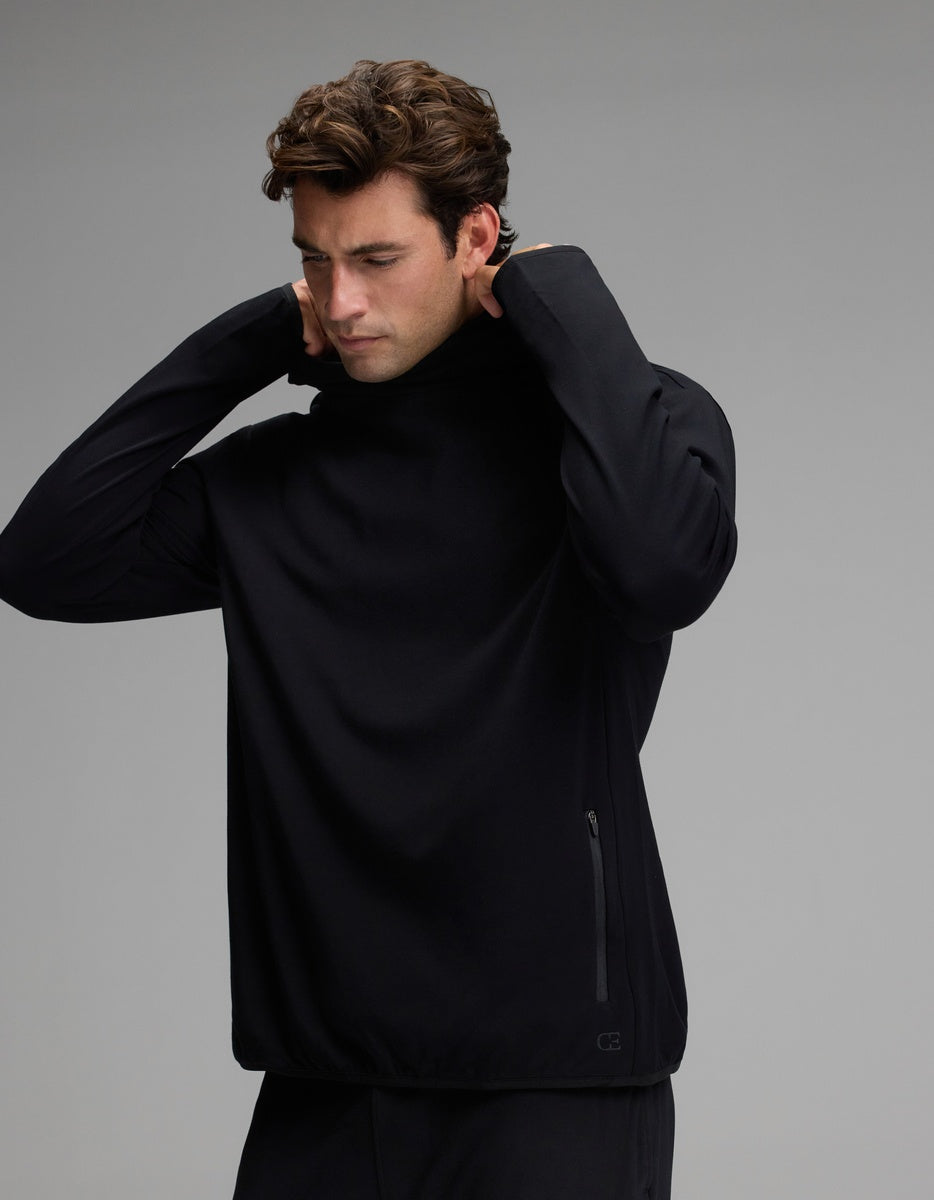 A man with wavy brown hair wears the Cozy Earth Men’s Recovery Hoodie in black, lifting its collar over his head. The background is plain gray, and the hoodie features a zippered pocket on the side.|Color:Black