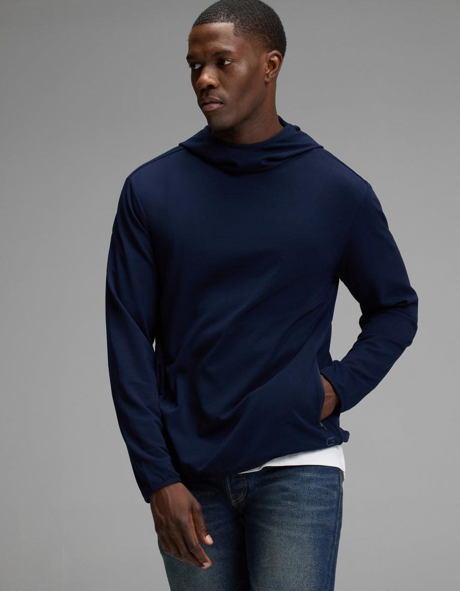 A person wearing the Cozy Earth Men’s Recovery Hoodie in navy stands against a plain gray background, with one hand in their pocket and looking slightly to the side.|Color:Navy