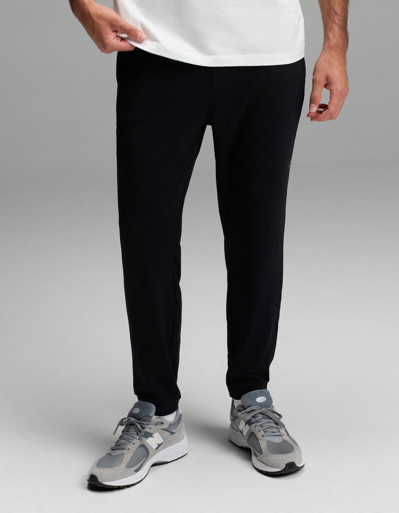 A person is shown from the waist down wearing Cozy Earth’s Men’s Recovery Jogger in black, standing against a plain gray background.
